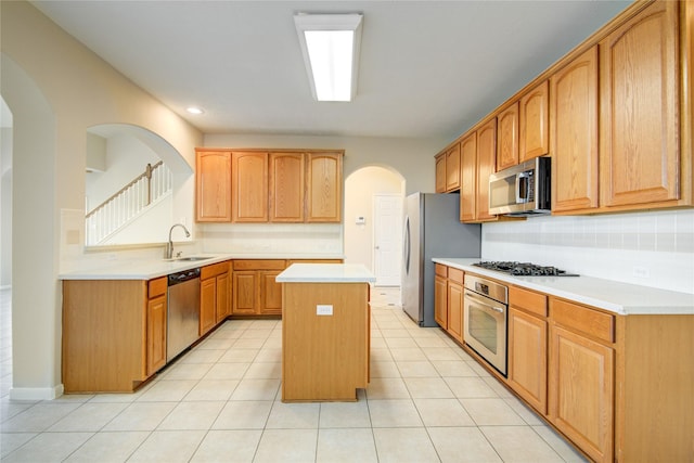 kitchen with light tile patterned floors, a sink, light countertops, appliances with stainless steel finishes, and a center island