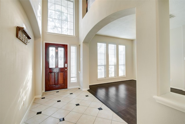 entryway featuring arched walkways, light tile patterned flooring, a high ceiling, and baseboards