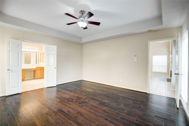 unfurnished bedroom featuring a ceiling fan, ensuite bathroom, baseboards, and wood finished floors