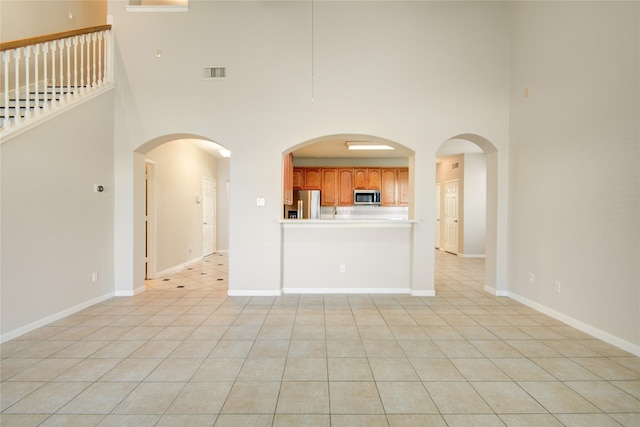 unfurnished living room with a high ceiling, light tile patterned flooring, visible vents, and baseboards