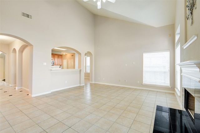 unfurnished living room featuring baseboards, visible vents, arched walkways, a tiled fireplace, and light tile patterned flooring