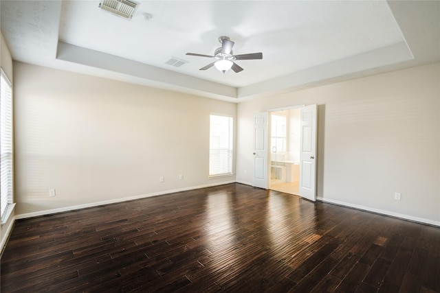 spare room with a tray ceiling, visible vents, and wood finished floors