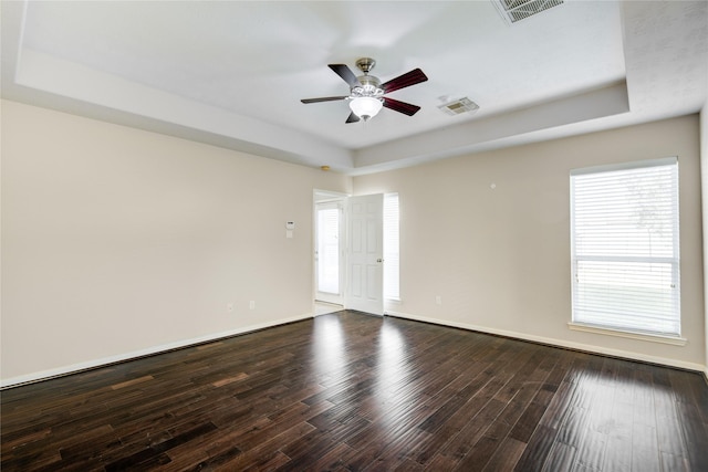 unfurnished room featuring a ceiling fan, a tray ceiling, dark wood-style flooring, and visible vents