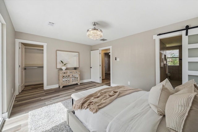 bedroom featuring light wood-style floors, a walk in closet, visible vents, and a barn door