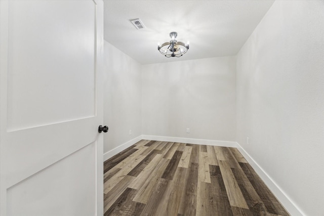 unfurnished dining area featuring baseboards, visible vents, a chandelier, and wood finished floors