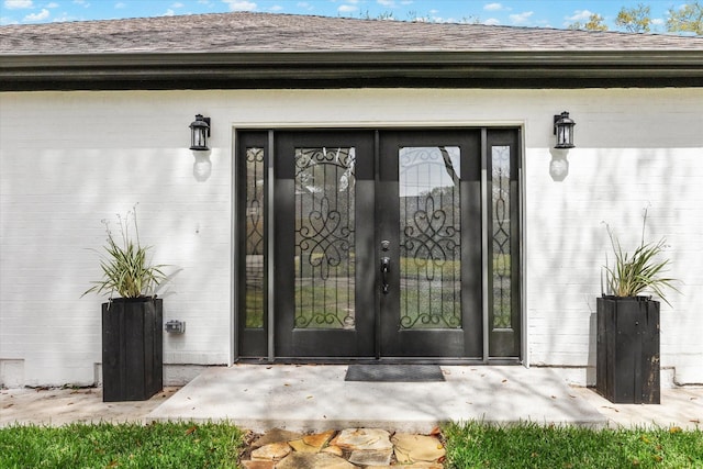 view of exterior entry with a shingled roof and brick siding