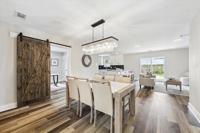 dining space featuring wood finished floors, visible vents, baseboards, and a barn door