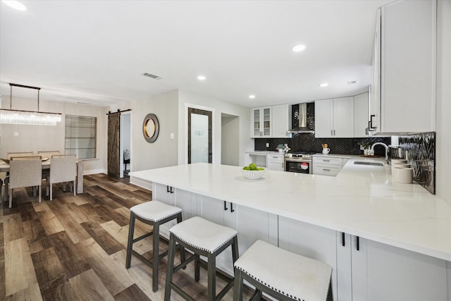 kitchen with a barn door, a sink, visible vents, stainless steel range oven, and wall chimney exhaust hood