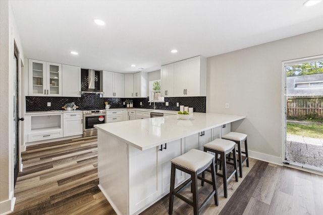 kitchen with tasteful backsplash, appliances with stainless steel finishes, wall chimney range hood, a peninsula, and a kitchen breakfast bar