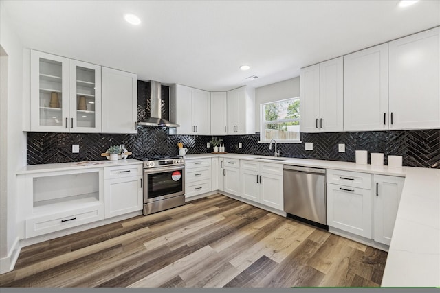 kitchen with light wood finished floors, stainless steel appliances, tasteful backsplash, a sink, and wall chimney exhaust hood