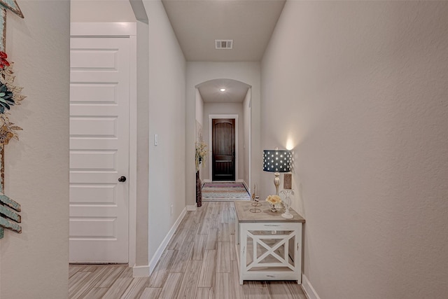 hallway featuring light wood-type flooring, visible vents, arched walkways, and baseboards