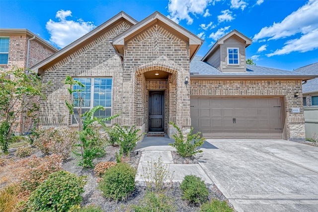 french country home featuring a garage, driveway, roof with shingles, and brick siding