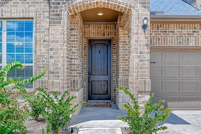 property entrance featuring an attached garage, a shingled roof, and brick siding