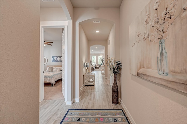 corridor with arched walkways, light wood finished floors, visible vents, and baseboards