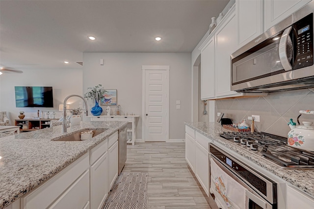 kitchen with light stone countertops, stainless steel appliances, a sink, white cabinets, and decorative backsplash