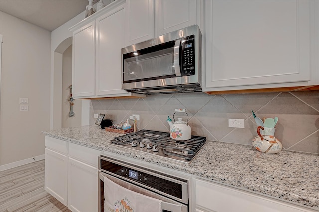 kitchen with light stone counters, stainless steel appliances, white cabinetry, baseboards, and backsplash