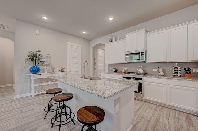 kitchen with arched walkways, a breakfast bar area, a sink, appliances with stainless steel finishes, and decorative backsplash