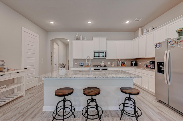 kitchen featuring arched walkways, stainless steel appliances, visible vents, a sink, and a kitchen bar