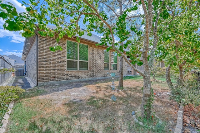 exterior space featuring brick siding, fence, and central AC