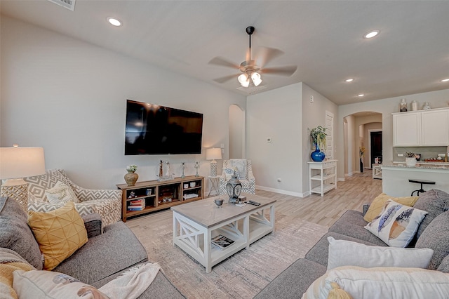 living room featuring light wood finished floors, baseboards, arched walkways, ceiling fan, and recessed lighting