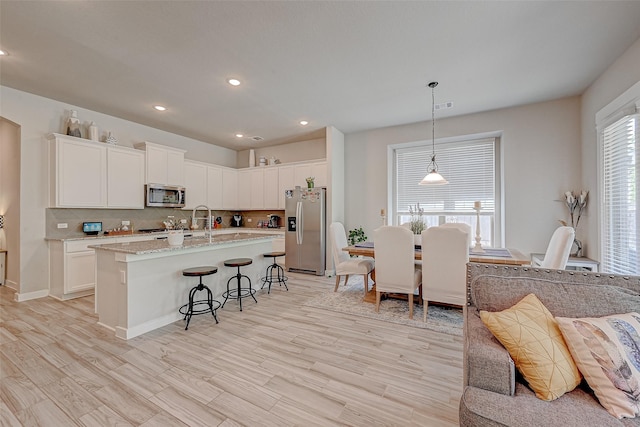 kitchen featuring a center island with sink, visible vents, appliances with stainless steel finishes, a kitchen bar, and backsplash