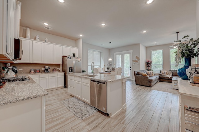 kitchen featuring decorative backsplash, appliances with stainless steel finishes, light wood-style floors, open floor plan, and a sink