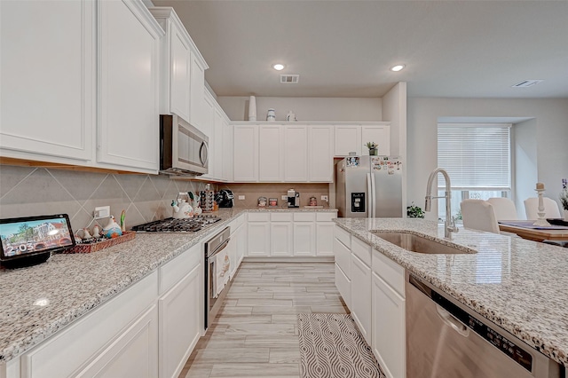 kitchen with stainless steel appliances, a sink, white cabinetry, visible vents, and decorative backsplash