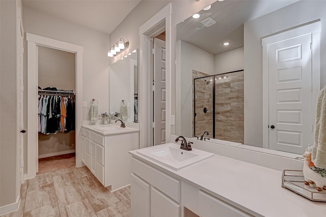 full bath featuring two vanities, a sink, baseboards, a stall shower, and a walk in closet