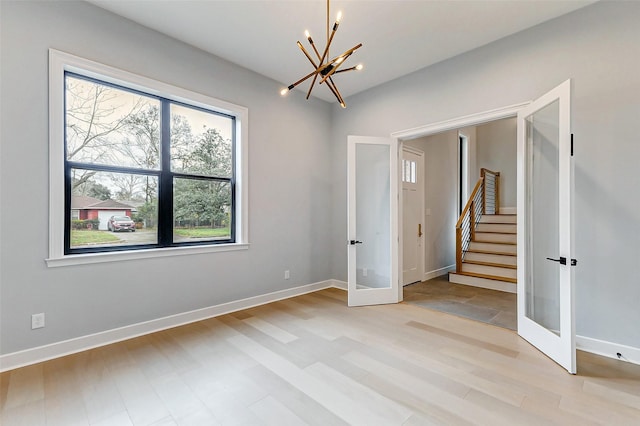 empty room featuring french doors, light wood-style flooring, stairway, a chandelier, and baseboards