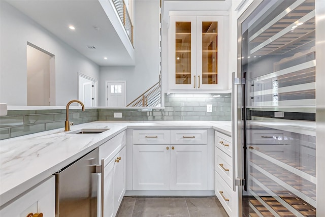 kitchen featuring light stone counters, wine cooler, backsplash, white cabinetry, and a sink