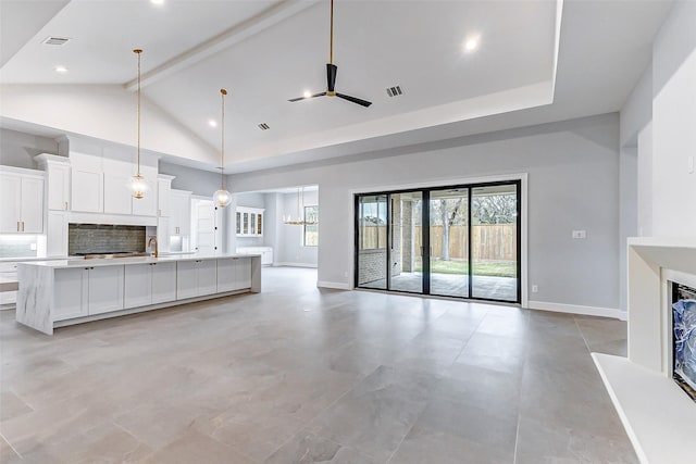 unfurnished living room with visible vents, a sink, high vaulted ceiling, beamed ceiling, and baseboards