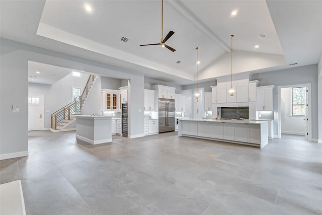 kitchen with high vaulted ceiling, stainless steel appliances, white cabinets, tasteful backsplash, and a large island with sink