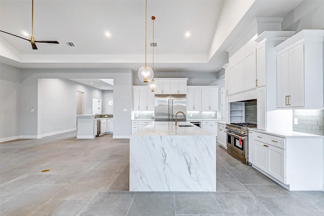 kitchen featuring a sink, visible vents, a tray ceiling, high end appliances, and a center island with sink