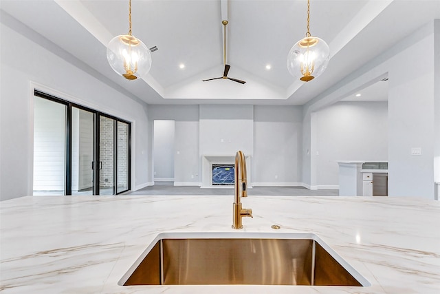 kitchen featuring open floor plan, a glass covered fireplace, a sink, and light stone counters