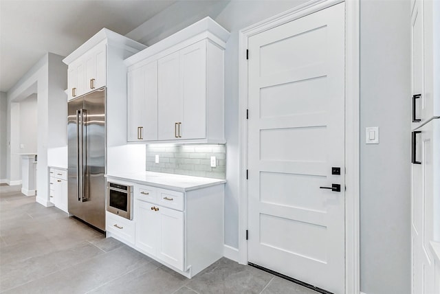 kitchen with stainless steel built in fridge, baseboards, white cabinets, light countertops, and decorative backsplash