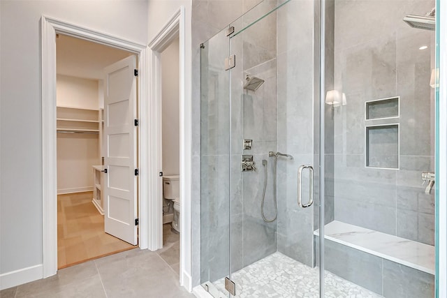 full bathroom with a walk in closet, toilet, a shower stall, baseboards, and tile patterned floors