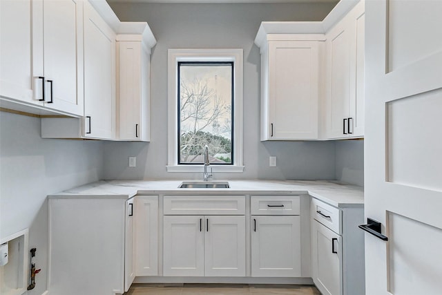 kitchen with white cabinetry, light stone counters, and a sink