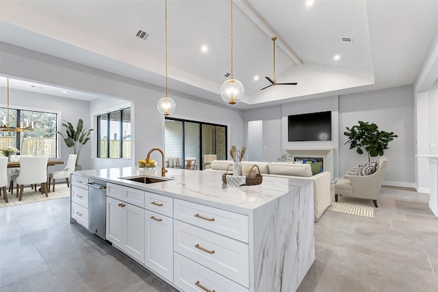 kitchen featuring visible vents, an island with sink, light stone countertops, white cabinetry, and a sink