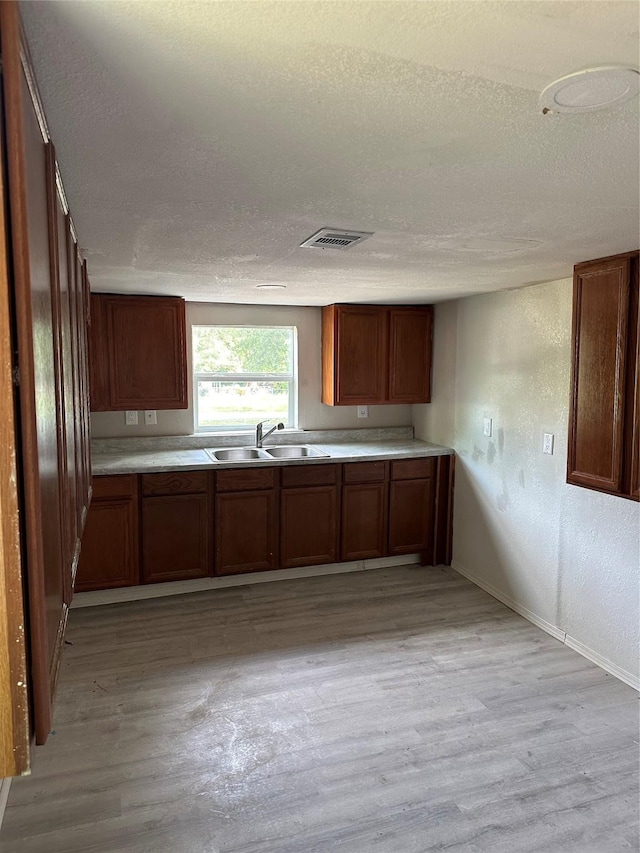 kitchen featuring light wood finished floors, a textured wall, brown cabinetry, a sink, and a textured ceiling