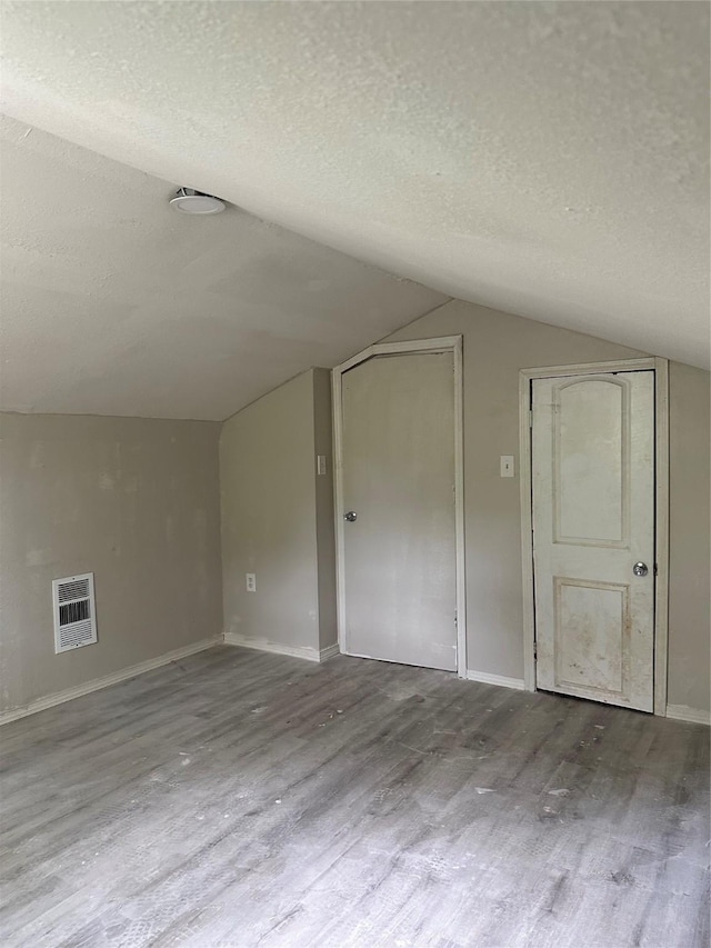 bonus room featuring a textured ceiling, baseboards, wood finished floors, and lofted ceiling