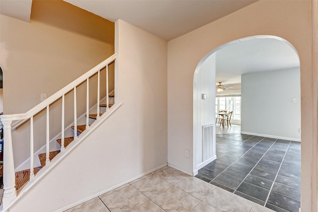 staircase featuring tile patterned floors, baseboards, arched walkways, and ceiling fan