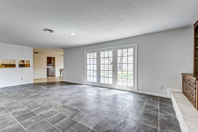 unfurnished living room featuring visible vents, baseboards, washer / clothes dryer, a textured ceiling, and dark tile patterned flooring