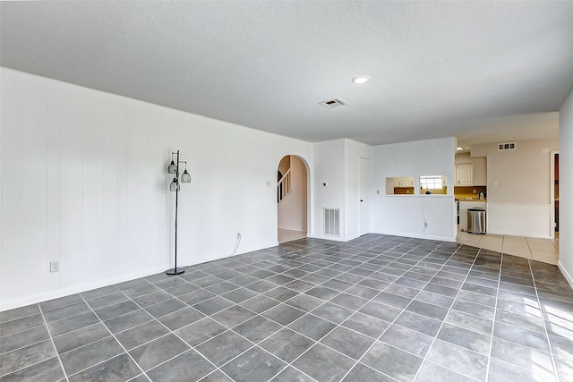 unfurnished living room featuring tile patterned floors, visible vents, and arched walkways