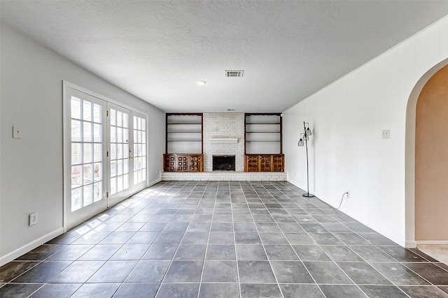 unfurnished living room featuring visible vents, a textured ceiling, arched walkways, tile patterned flooring, and a brick fireplace