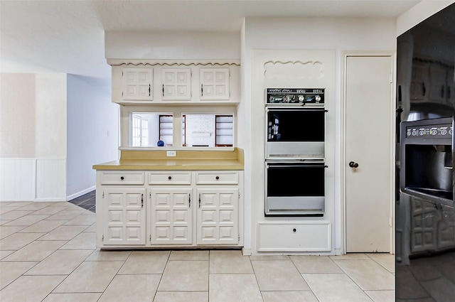 kitchen with light tile patterned flooring, wainscoting, white cabinets, white double oven, and light countertops