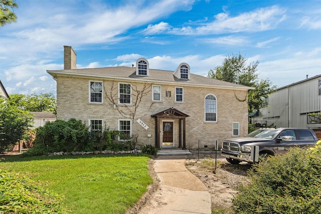 view of front of house with brick siding, a chimney, and a front yard