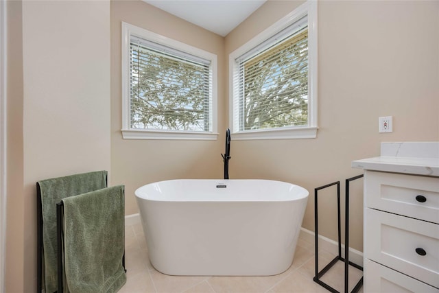 full bathroom with tile patterned flooring, a soaking tub, vanity, and baseboards