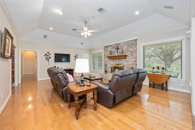 living room with a tray ceiling, light wood-style flooring, a fireplace, ornamental molding, and vaulted ceiling