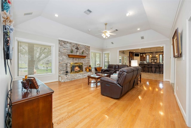 living area featuring light wood finished floors, visible vents, a brick fireplace, a tray ceiling, and vaulted ceiling