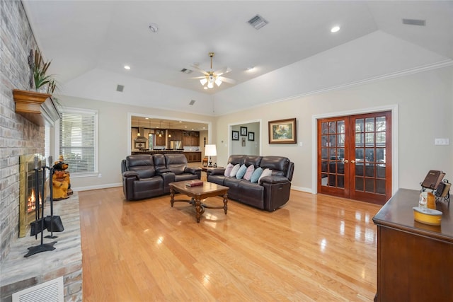 living room featuring light wood finished floors, visible vents, a brick fireplace, french doors, and a raised ceiling